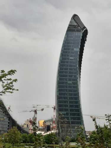 Generali Tower in CityLife Milaan, ontworpen door Zaha Hadid, gezien vanaf het centrale park met op de achtergrond bouwkranen en nieuwe stedelijke ontwikkeling.